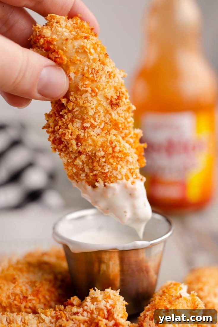 Closeup of fingers dipping a chicken strip into sauce with more strips nearby.