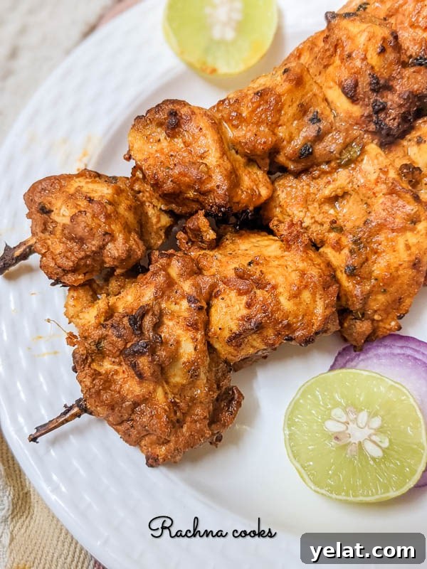 Two skewers of chicken tikka on a white plate with lime and red onion.