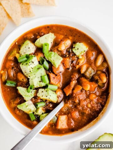 Vegetarian chili with avocado in a white bowl with a silver spoon.