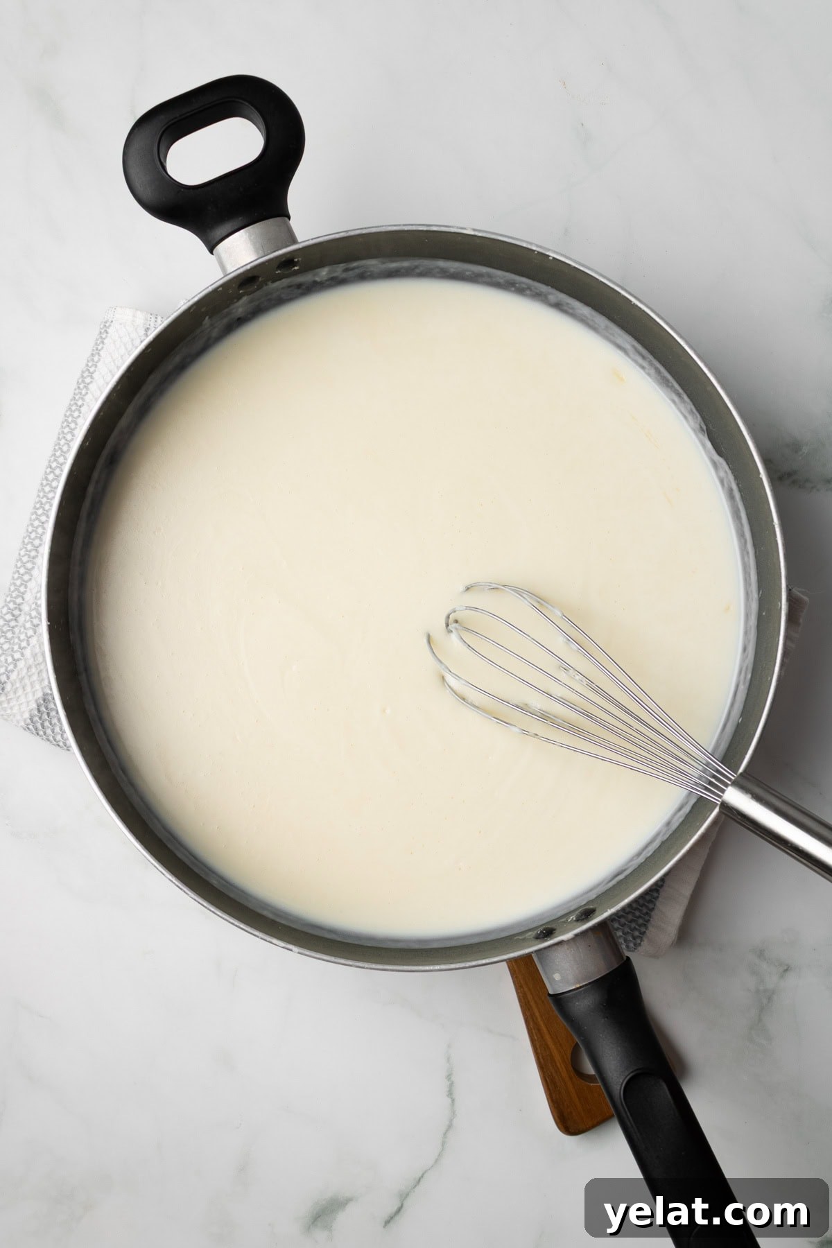 An overhead image of whisking the bechamel sauce together in a pan.