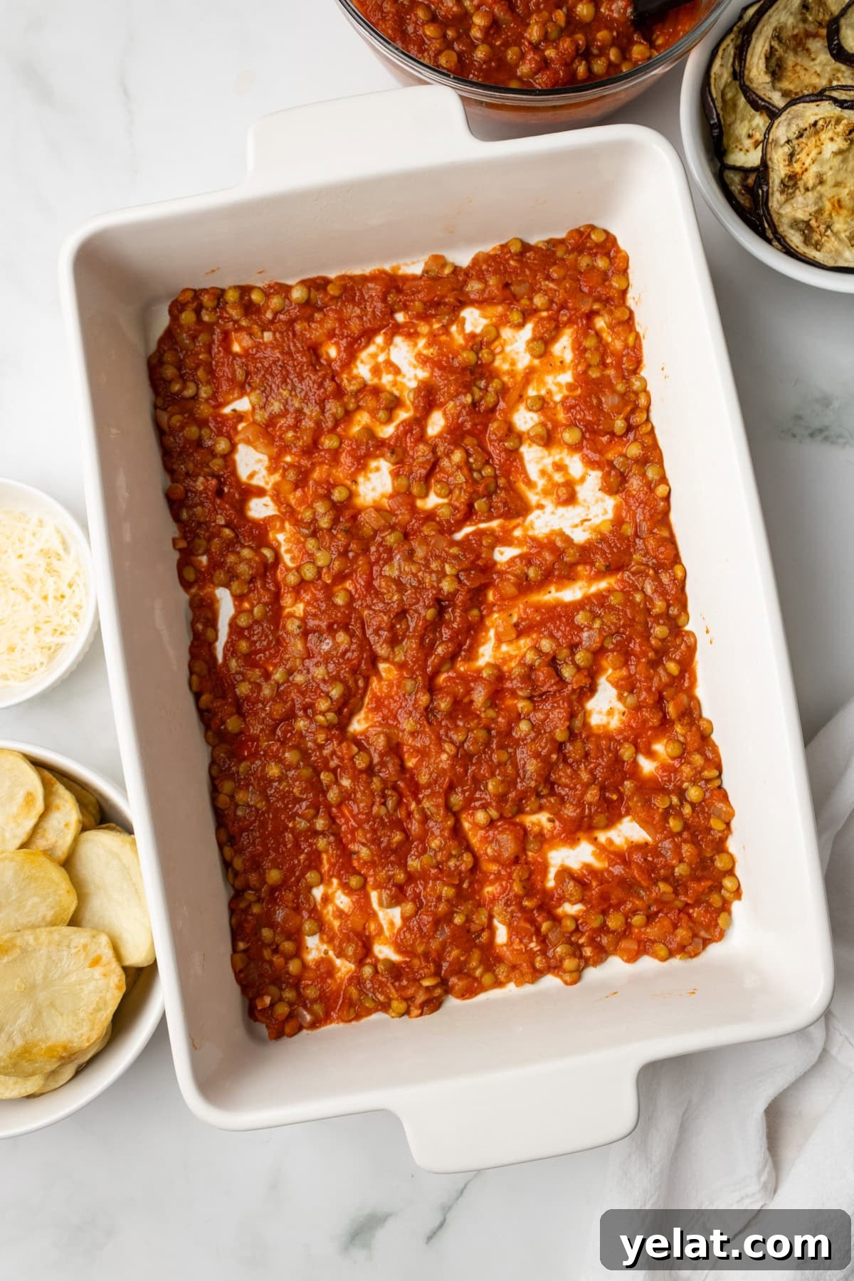 An overhead image of spreading lentil tomato sauce on the bottom of the baking dish.