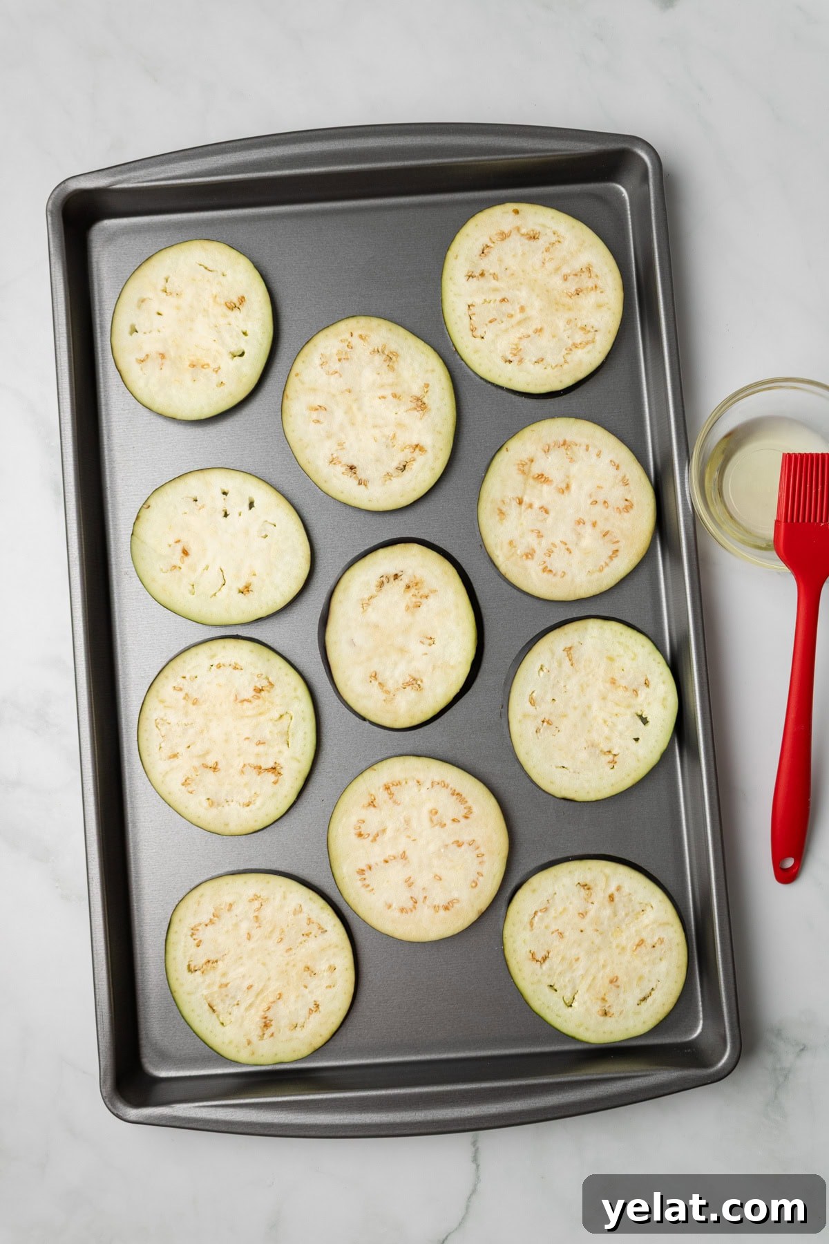 An overhead image of arranging eggplants on a baking sheet.