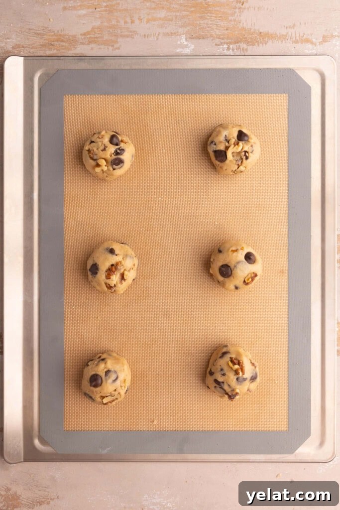 Chocolate chip walnut cookie dough shaped and spaced out on a lined cookie sheet.