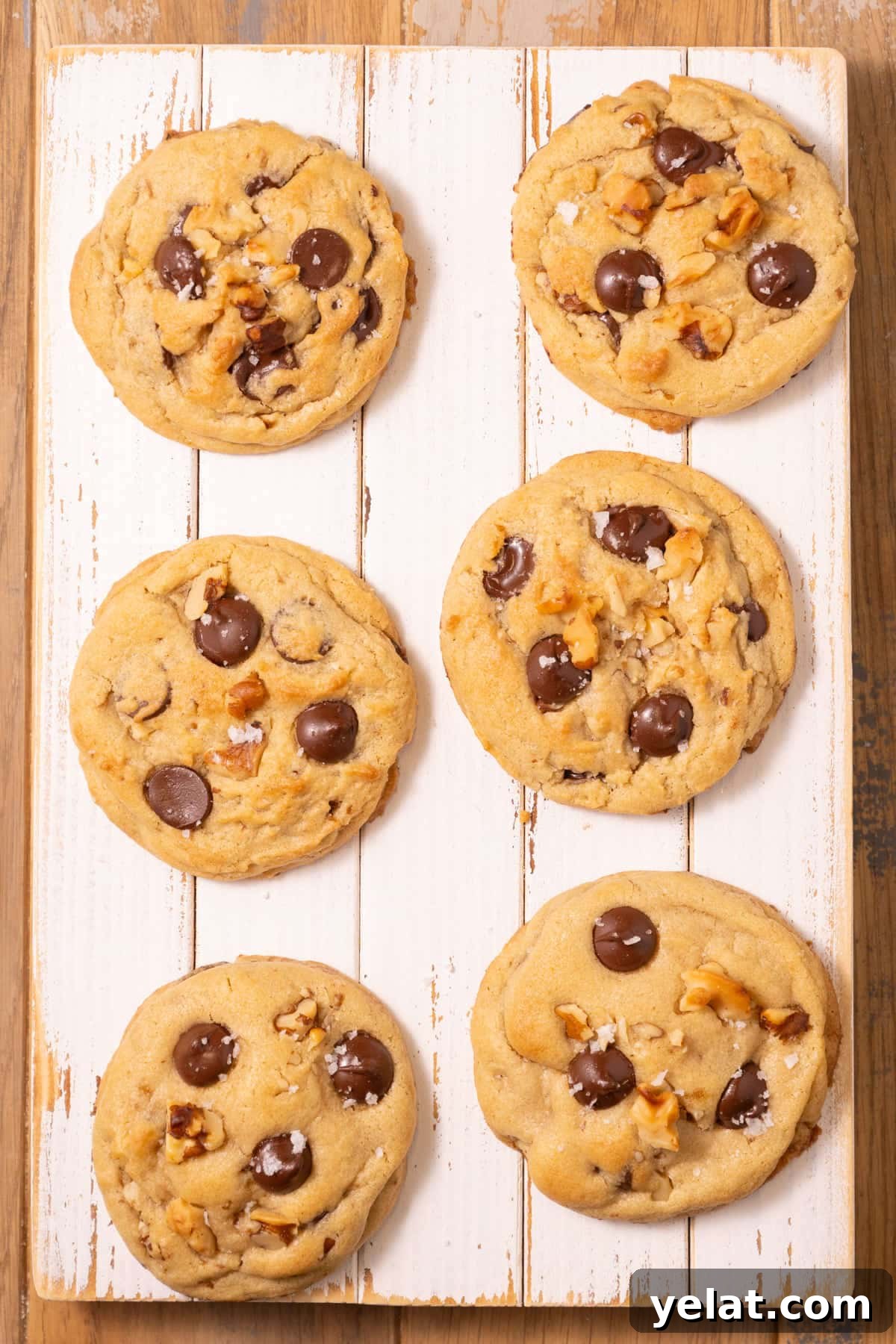 Homemade walnut chocolate chip cookies lined up on a white wooden board.