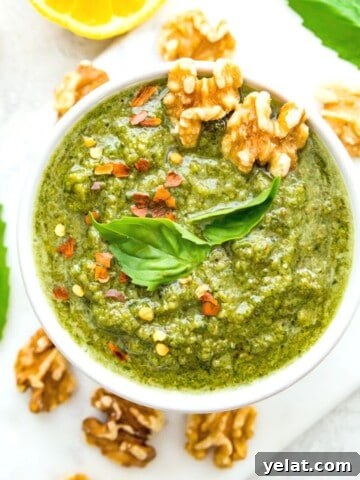 A bowl of vegan walnut pesto topped with fresh basil leaves and walnuts.