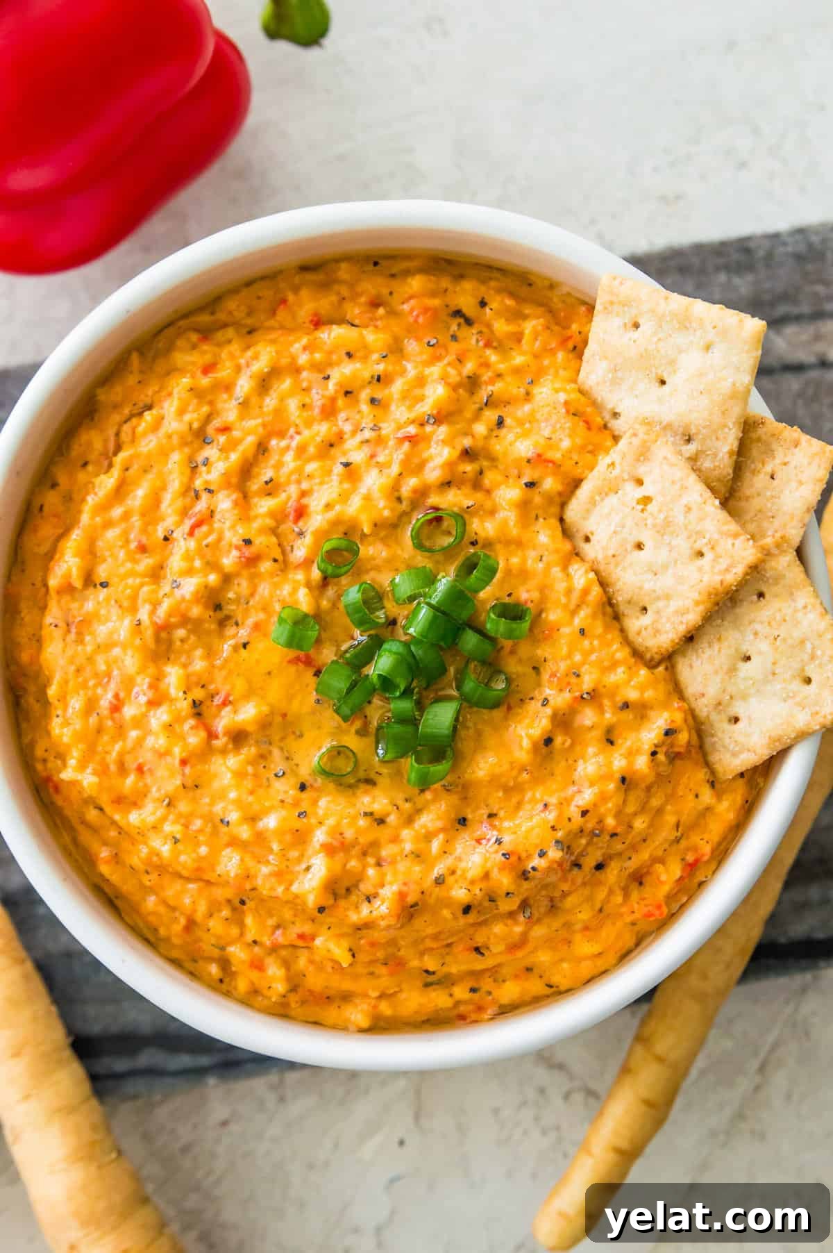 Roasted Red Pepper Cashew-Parsnip Dip (Vegan) 9 A bowl with an orange dip in it topped with chopped green onion and crackers in it.