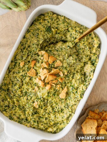 A white casserole dish filled with a vegan spinach artichoke dip with crushed crackers on top.