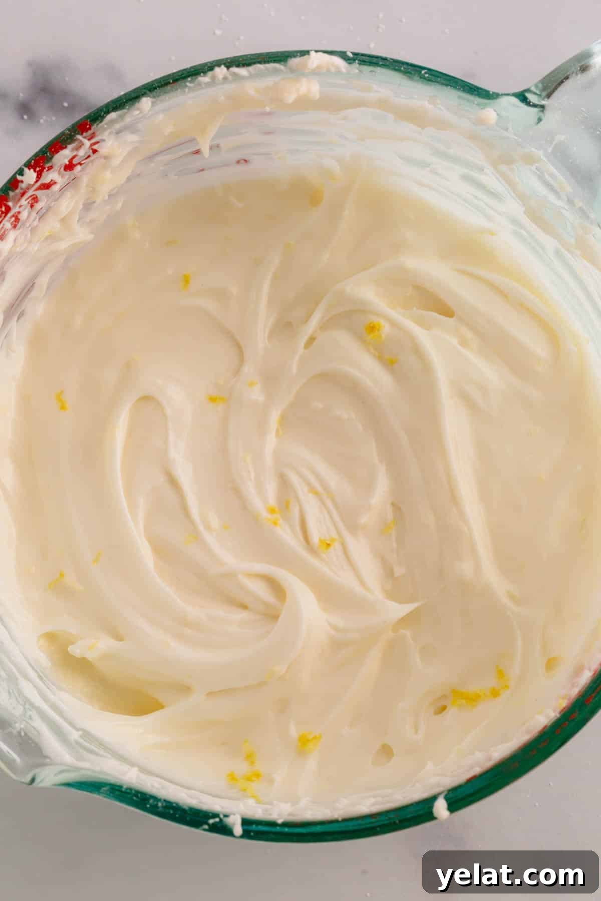 Lemon Sheet Cake Recipe: Zesty, Moist Lemon Cake for Large Groups 10 A liquid measuring cup full of lemon cream cheese frosting with flakes of lemon zest.