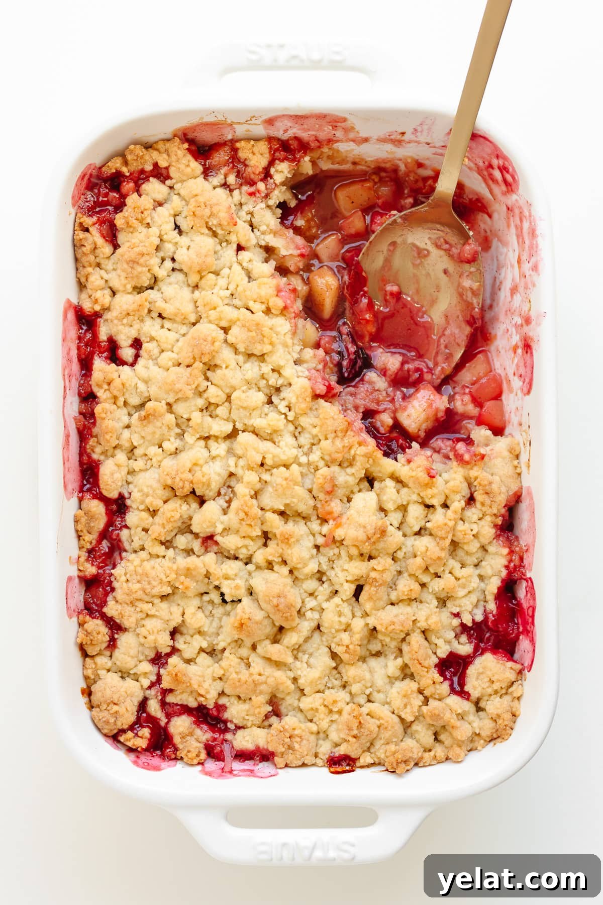Rustic Plum & Apple Crumble Recipe for Fall Baking 2 Plum apple crumble in a white baking dish with a serving spoon sitting in a corner where a portion has been scooped out.