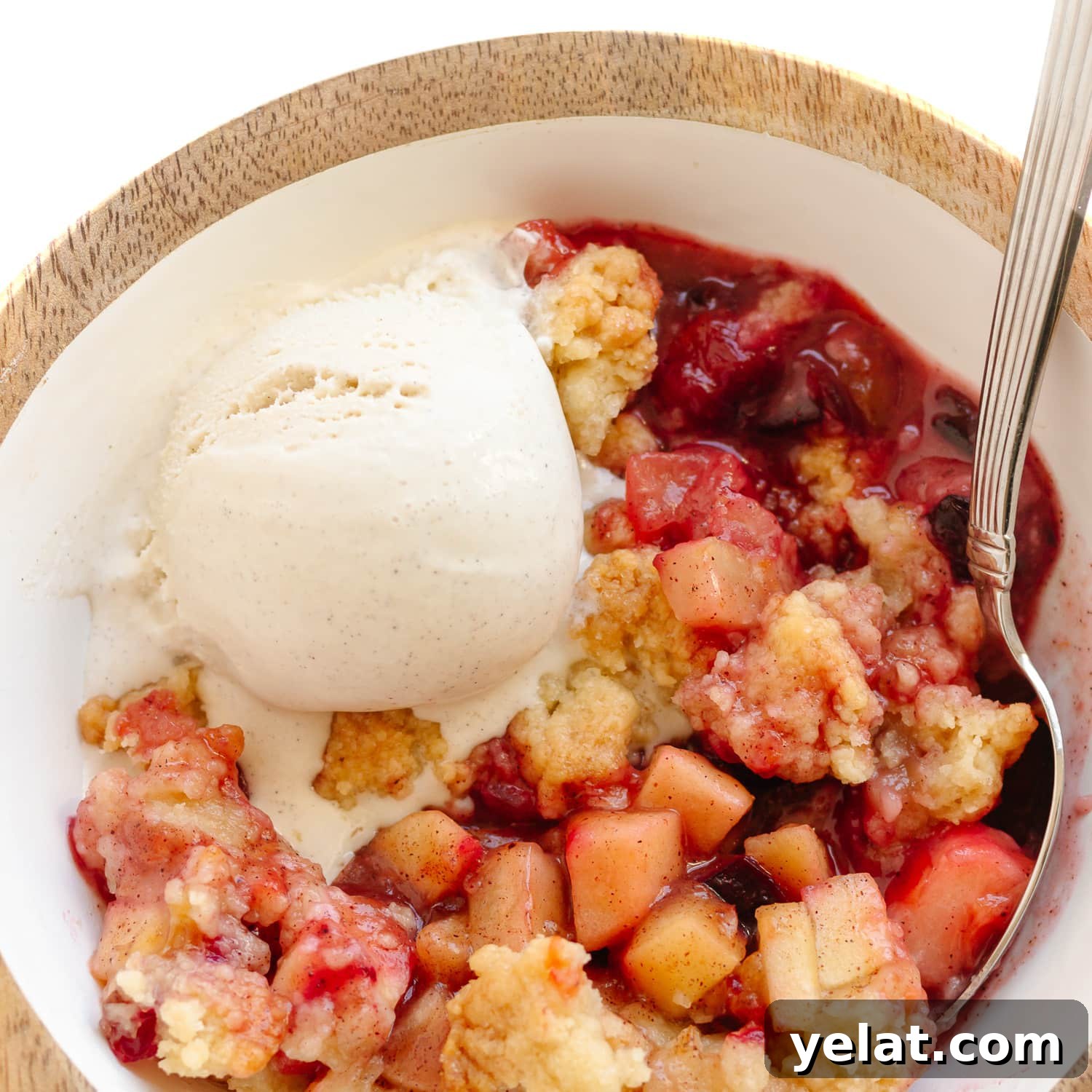 Rustic Plum & Apple Crumble Recipe for Fall Baking 11 Bowl of plum and apple crumble with a spoon and scoop of vanilla ice cream melting on top.