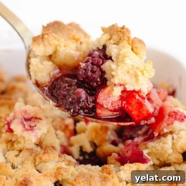 Rustic Plum & Apple Crumble Recipe for Fall Baking 14 Serving spoon scooping up some apple and blackberry crumble from the baking dish.