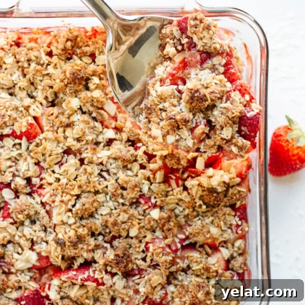 Rustic Plum & Apple Crumble Recipe for Fall Baking 15 Serving spoon digging into a square glass dish of Strawberry Coconut Crisp.
