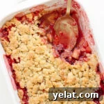 Plum and apple crumble in a white baking dish with a portion scooped out.