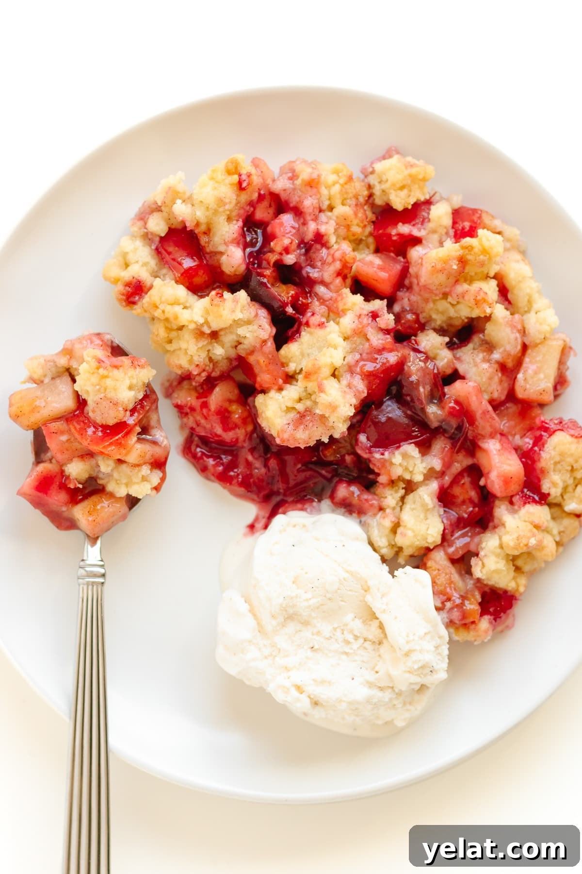 Rustic Plum & Apple Crumble Recipe for Fall Baking 3 Plum and apple crumble on a white plate with a scoop of vanilla ice cream and spoon.