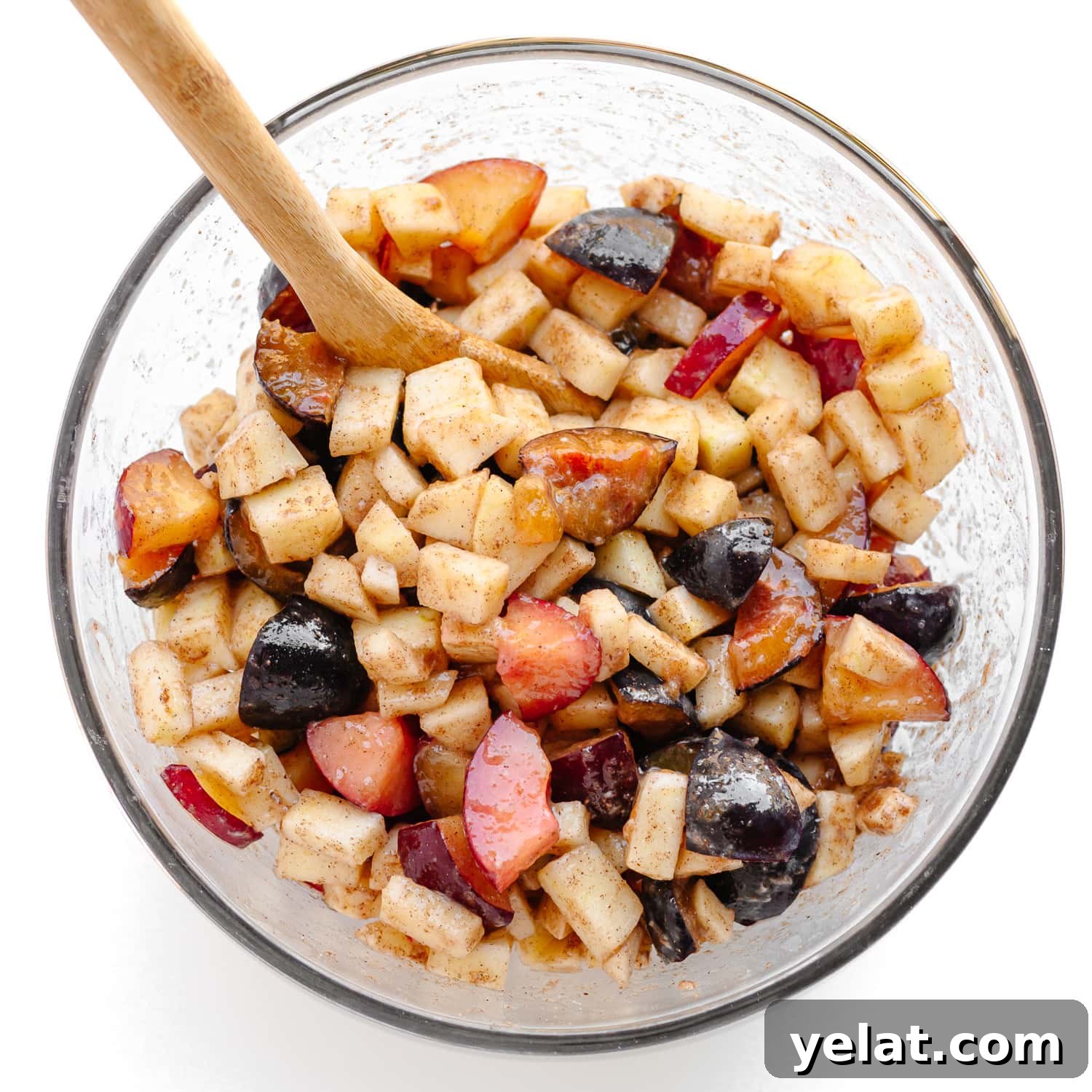 Rustic Plum & Apple Crumble Recipe for Fall Baking 5 Plum and apple fruit mixture for crumble being mixed in a glass bowl with a wooden spoon.