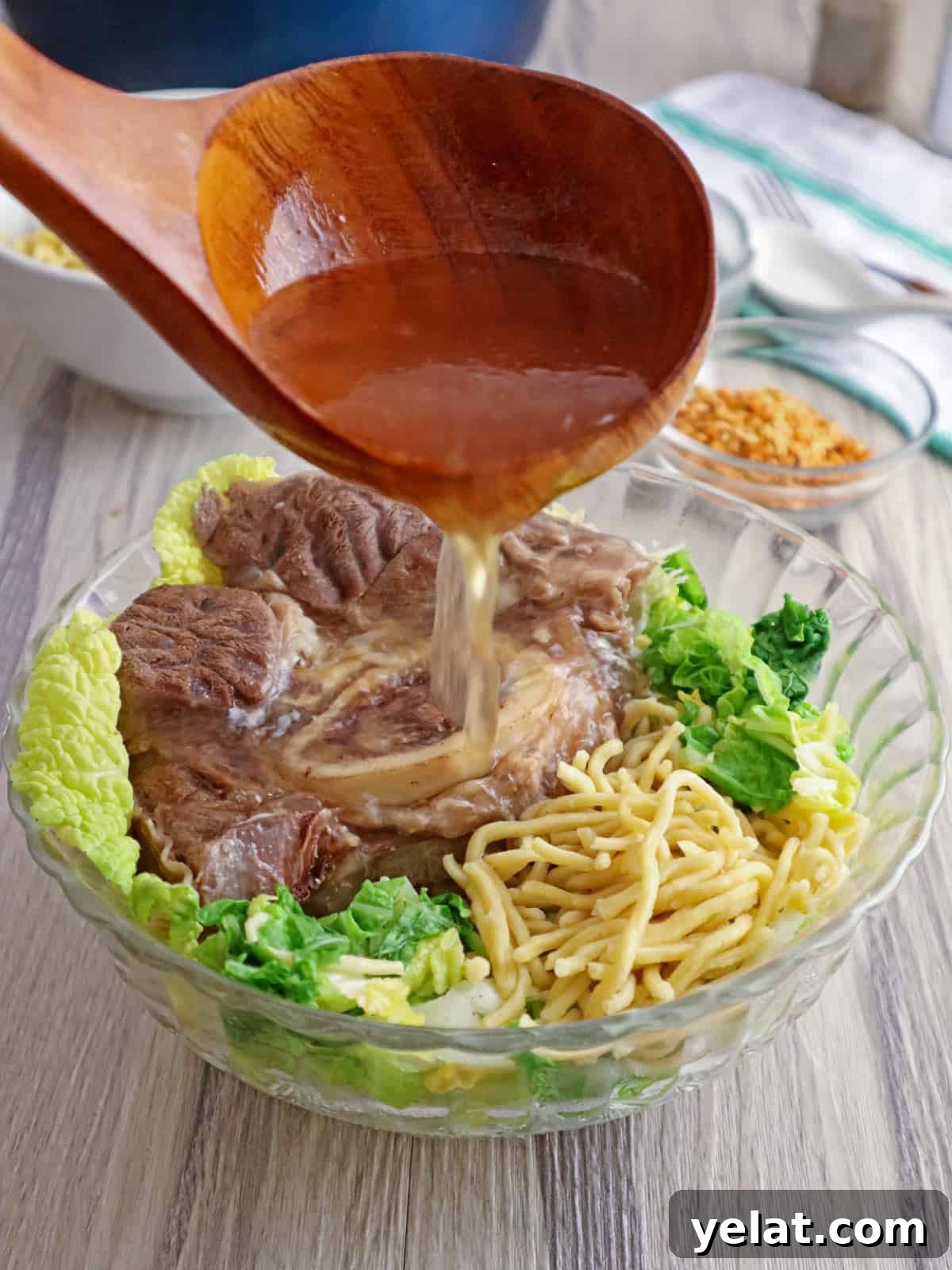 pouring hot broth to a bowl of beef, noodles, and cabbage