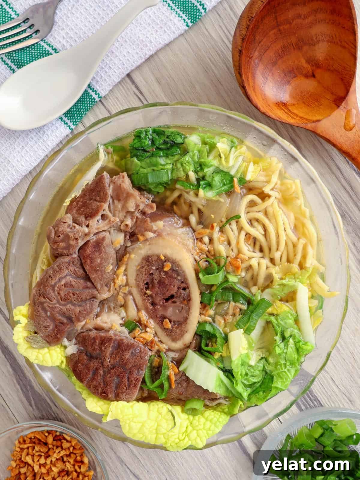 Bulalo Mami in a bowl with fried garlic bits and chopped green onions on the side