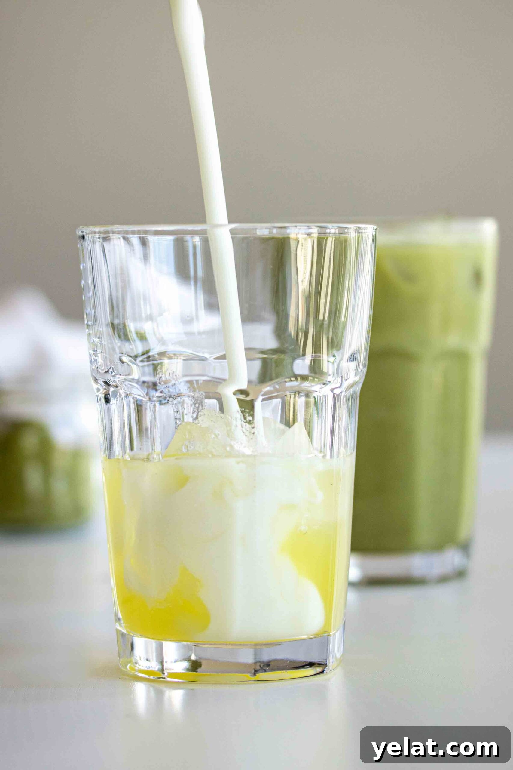 Coconut milk being poured over syrup in a glass full of ice
