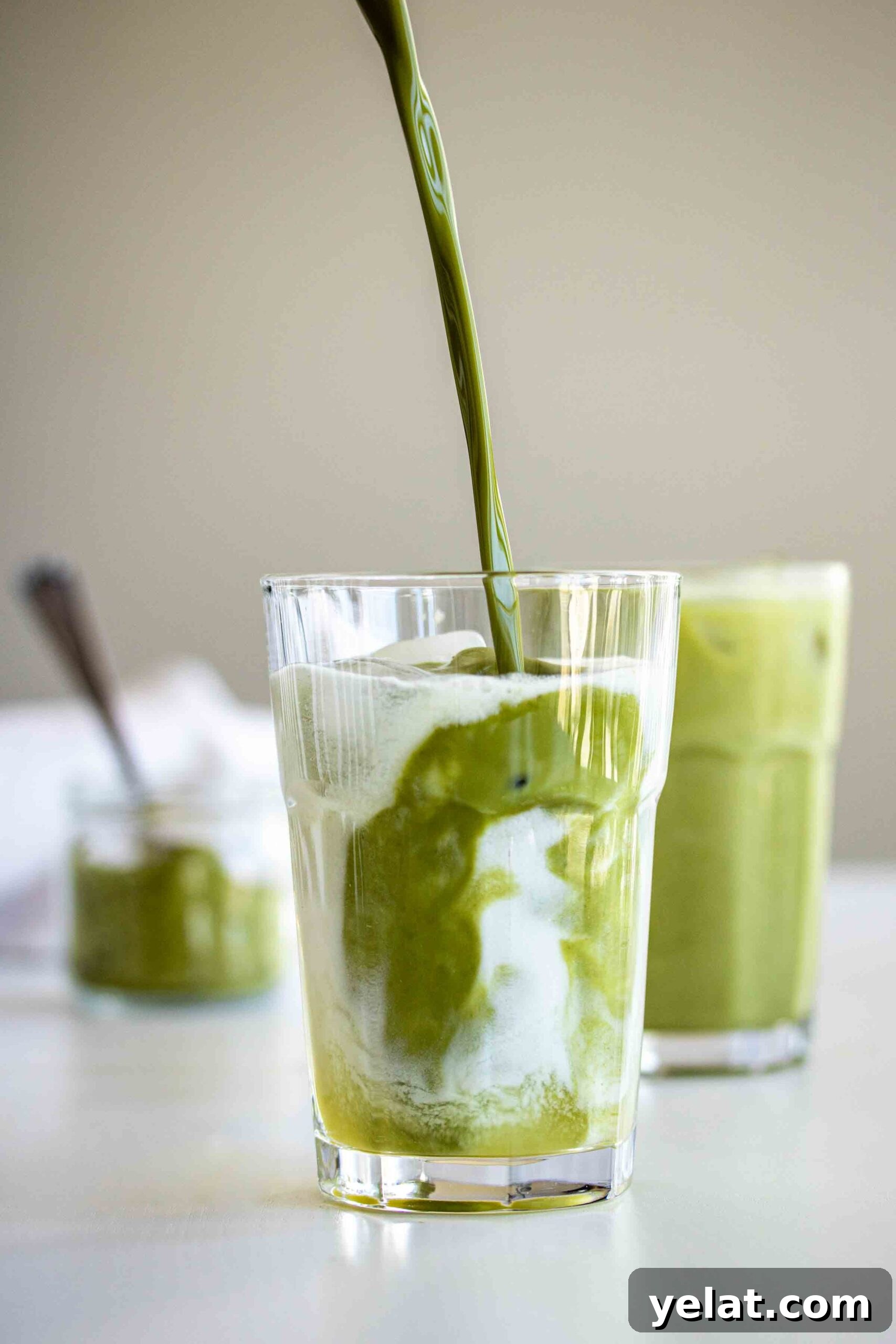 Matcha being poured in a glass with ice cubes, coconut milk and pineapple ginger syrup