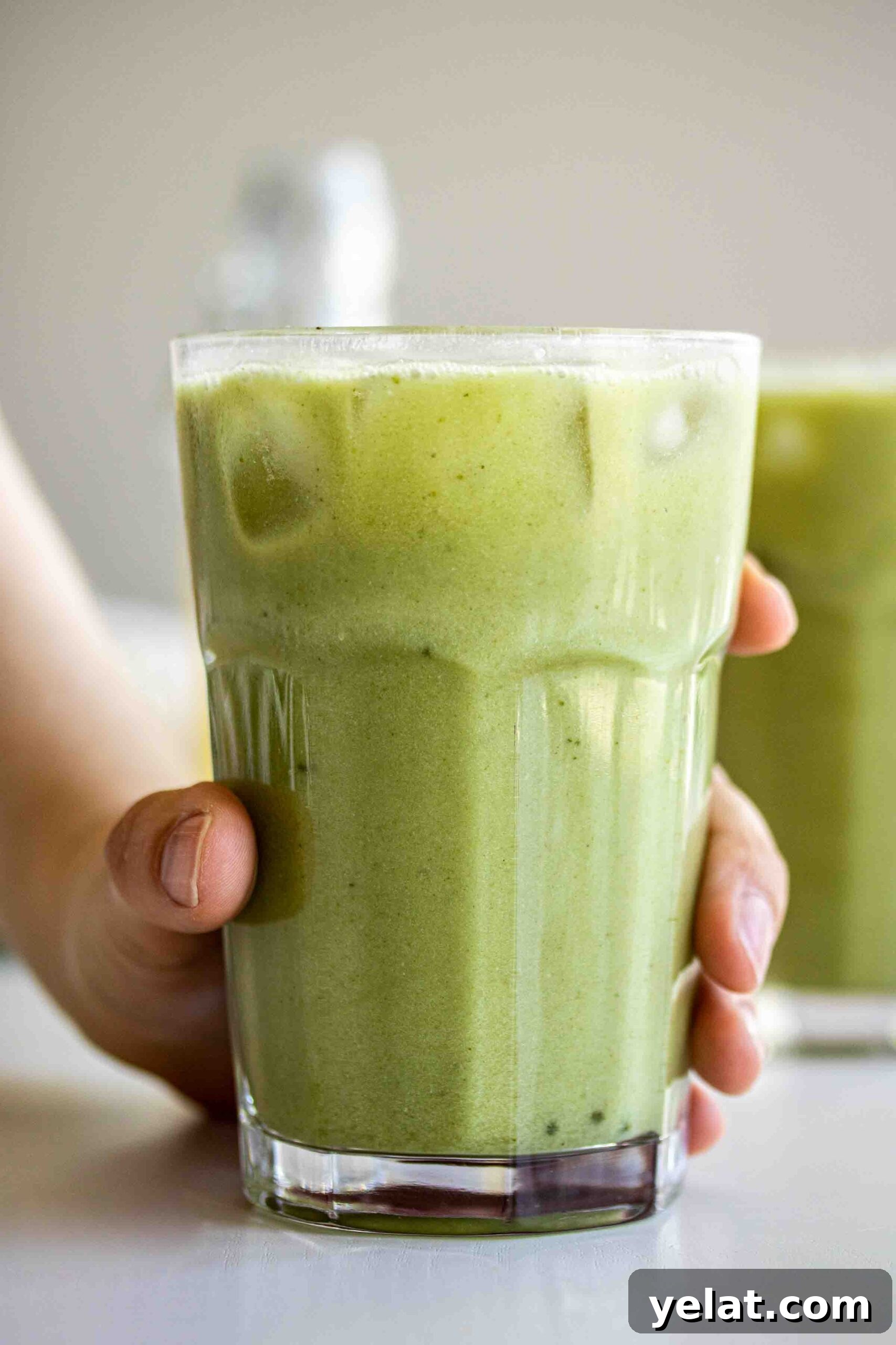 Hand holding a glass full of matcha pineapple ginger drink