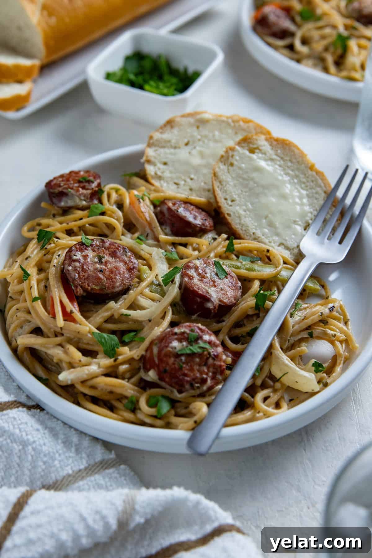 Cajun Sausage Spaghetti Recipe: Spicy Pasta with Andouille 2 Cooked cajun sausage spaghetti on white plate with a fork and two slices of buttered French bread on the side.