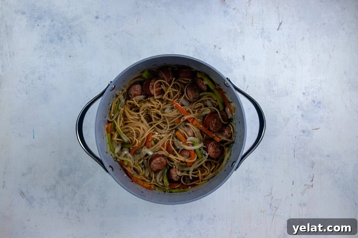 Cajun Sausage Spaghetti Recipe: Spicy Pasta with Andouille 6 Sausage, onions, and peppers in the pot with broth, seasonings, and raw spaghetti.