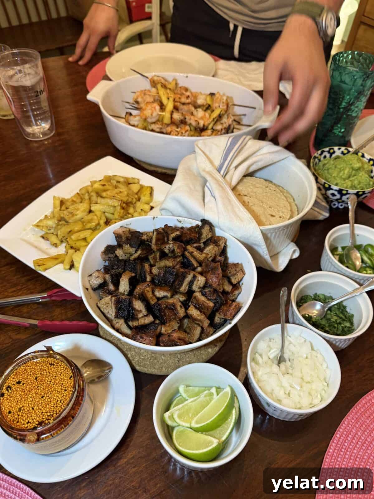 A table set for a meal with grilled meat, flatbreads, guacamole, lime wedges and a drink.