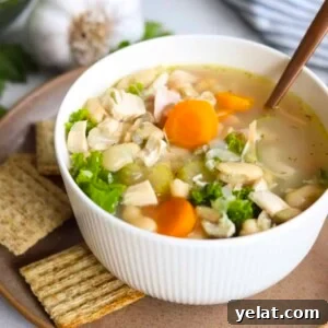 Hearty White Bean and Chicken Soup with Garlic and Herbs 15 small white bowl filled with chicken and white bean soup on a plate with crackers
