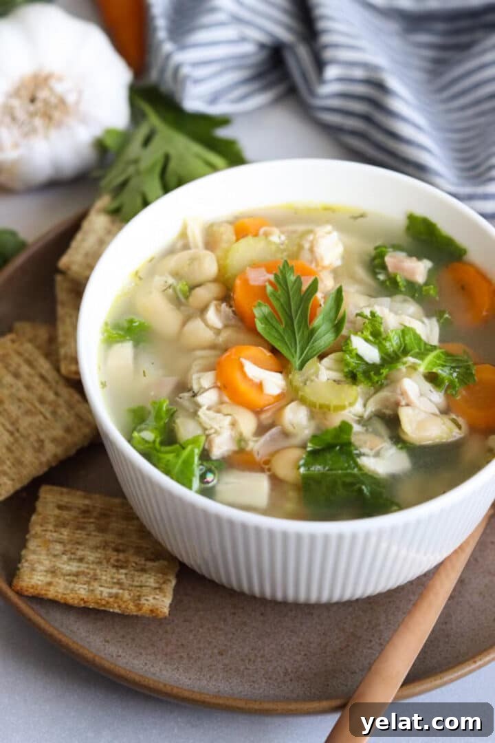 Hearty White Bean and Chicken Soup with Garlic and Herbs 9 Bowl of chicken and white bean soup with a gold spoon and crackers sitting next to it
