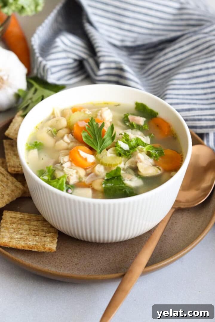 Hearty White Bean and Chicken Soup with Garlic and Herbs 10 Small white bowl with chicken and white bean soup, sitting next to triscuit crackers and a gold spoon