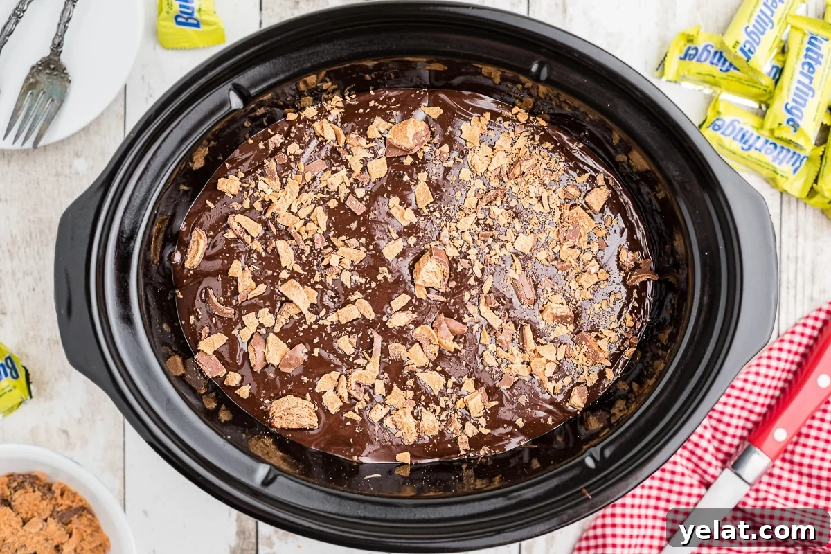 Slow Cooker Butterfinger Dessert Cake Recipe 5 overhead shot of butterfinger cake with hot fudge topping in crockpot.