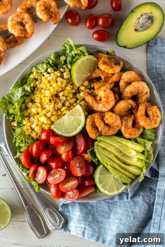 Grilled Shrimp, Avocado & Corn Salad with Lime Vinaigrette 2 Top down shot of grilled shrimp and corn salad in a bowl with tomatoes, avocado, and slices of lime.
