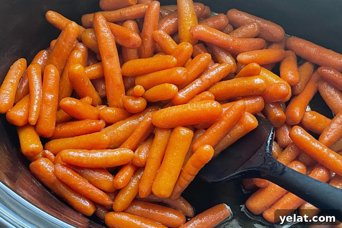 12 Crowd-Pleasing Easter Crockpot Recipes for a Stress-Free Holiday 10 A close-up view of shiny glazed baby carrots in a black cooking pot with a black spatula.