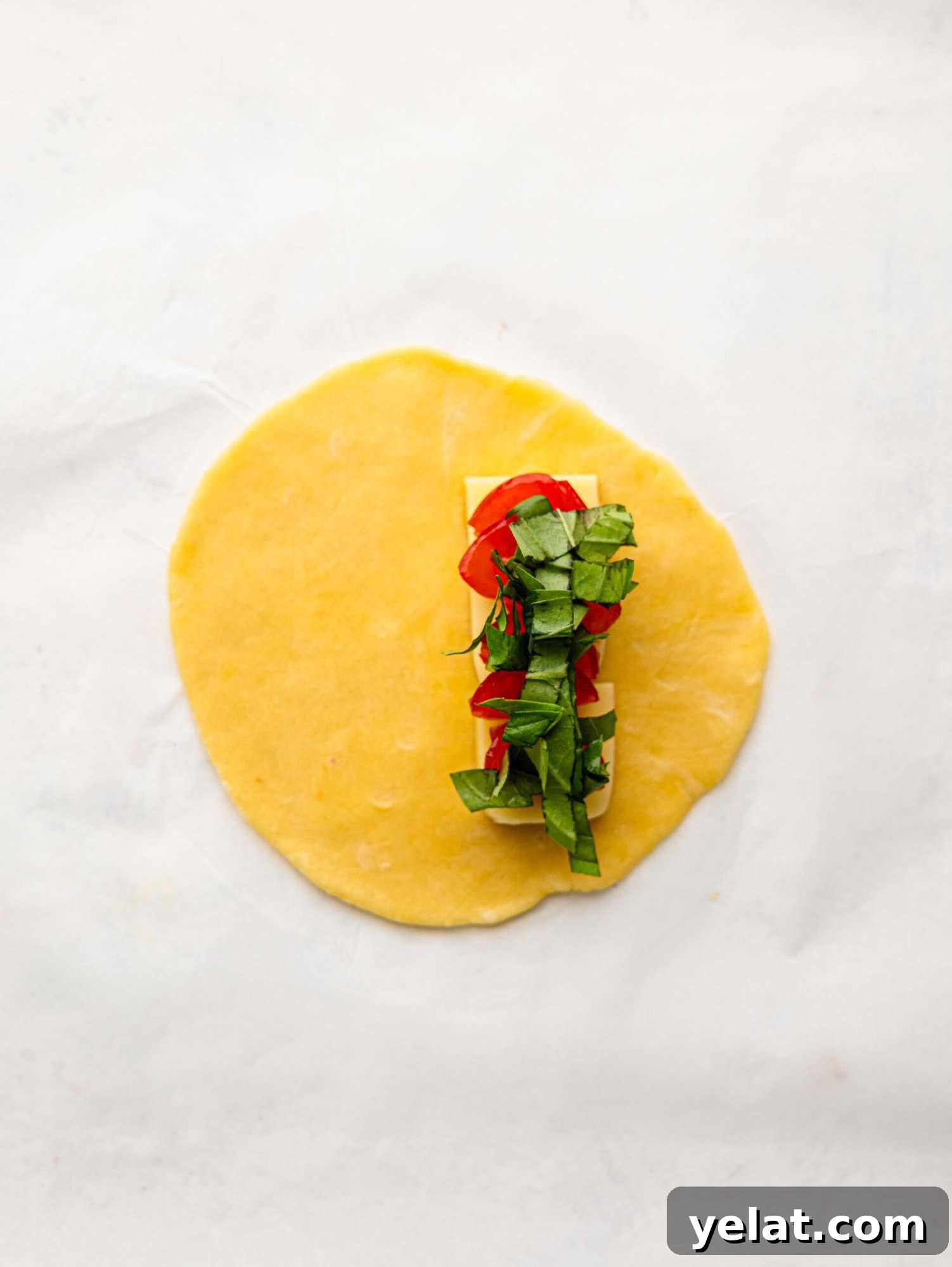 An empanada disk with mozzarella, tomatoes and basil on a sheet of parchment paper.