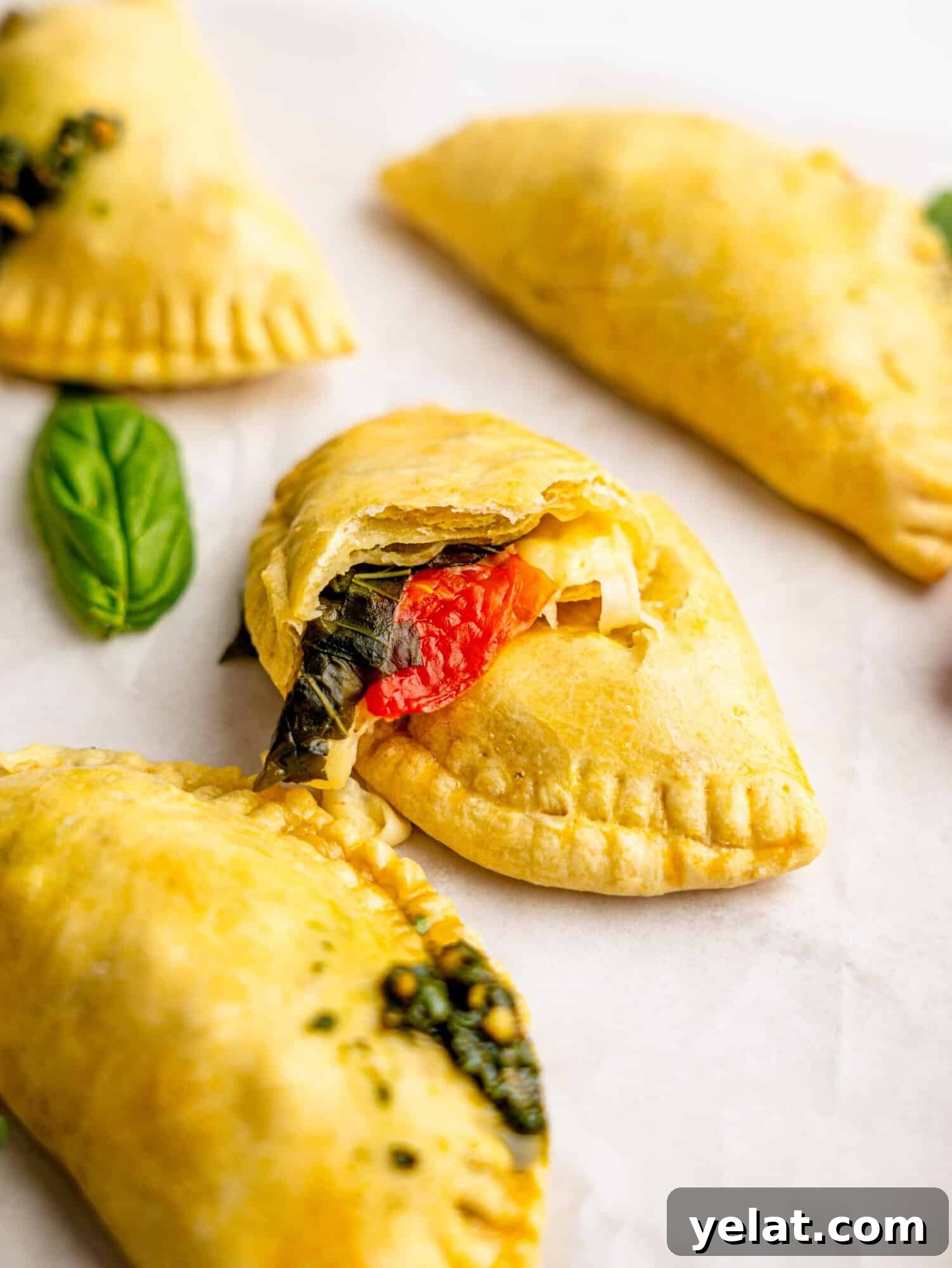 A caprese empanada torn in half revealing melted mozzarella, tomatoes and basil.