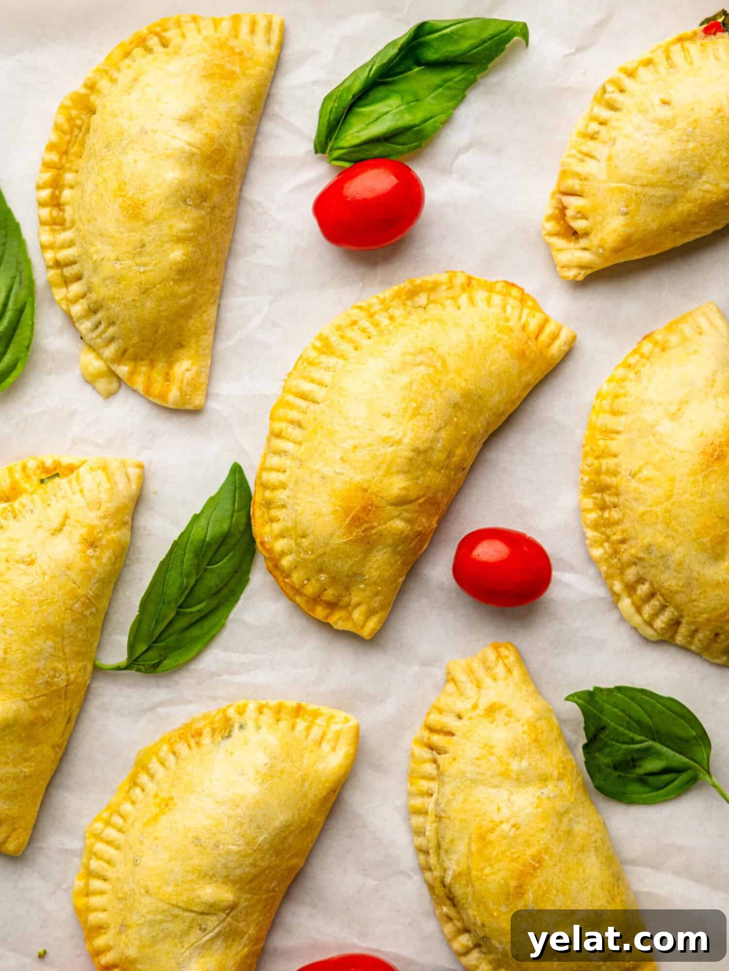 Caprese empanadas on a sheet of parchment paper with tomatoes and basil.
