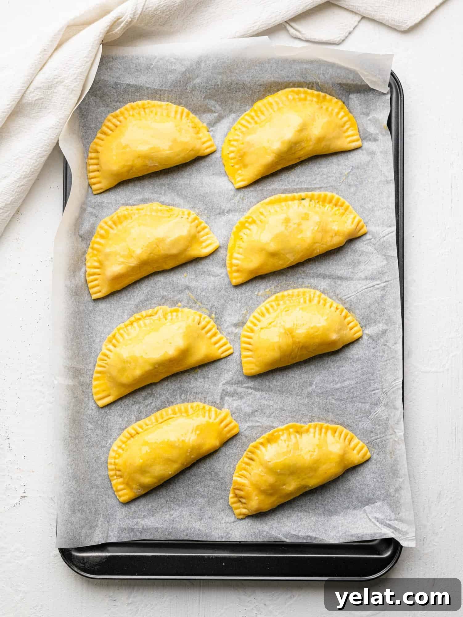 Eight caprese empanadas on a baking sheet before being baked.