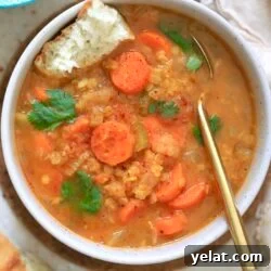 orange bowl of soup with carrots and gold spoon