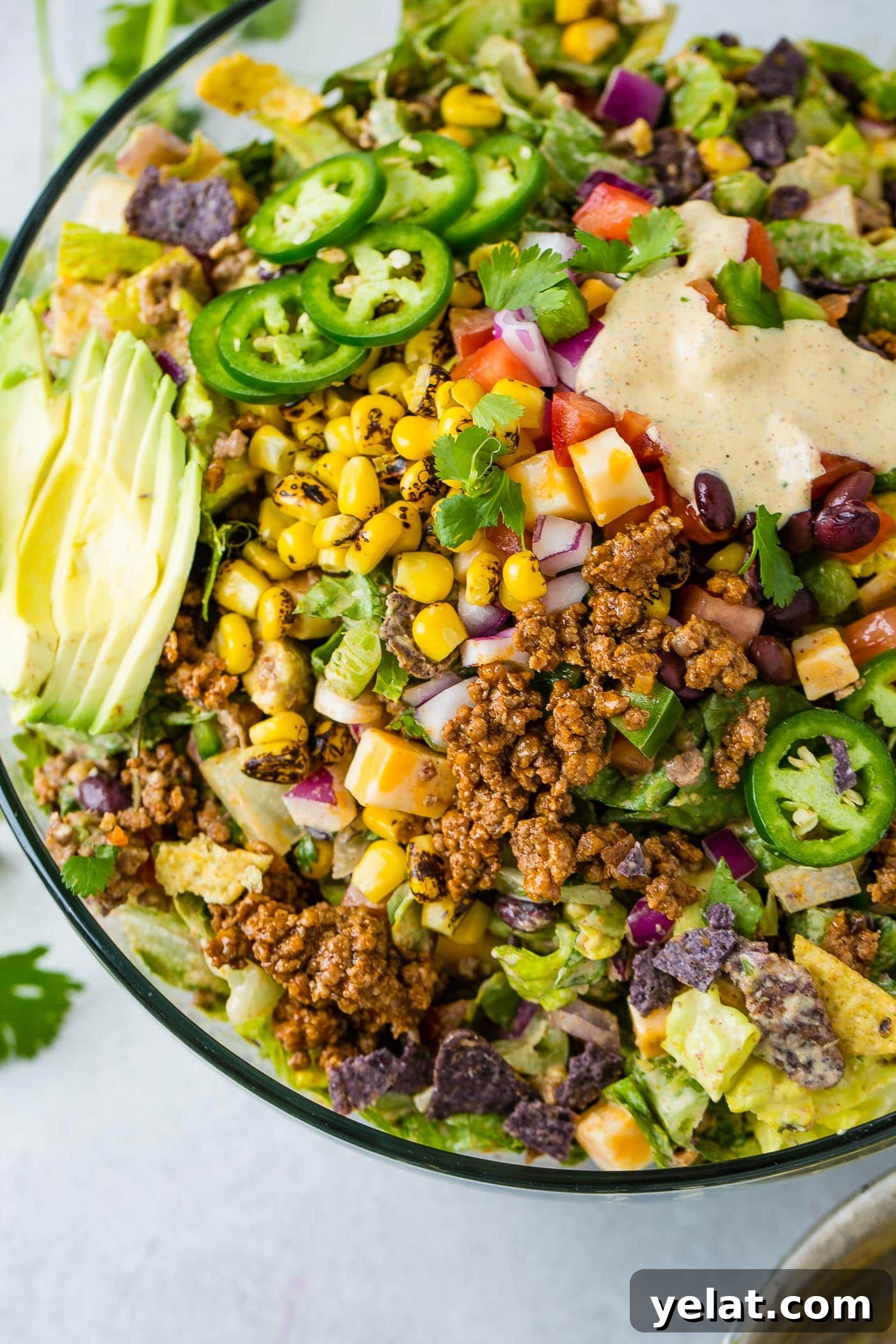 Tex-Mex Chopped Ground Beef Taco Salad Recipe 11 A large bowl of tex‑mex taco salad. It is loaded with tomatillos, lettuce, roasted corn, cilantro, meat, and chips. a little dressing is in the upper corner of the salad.