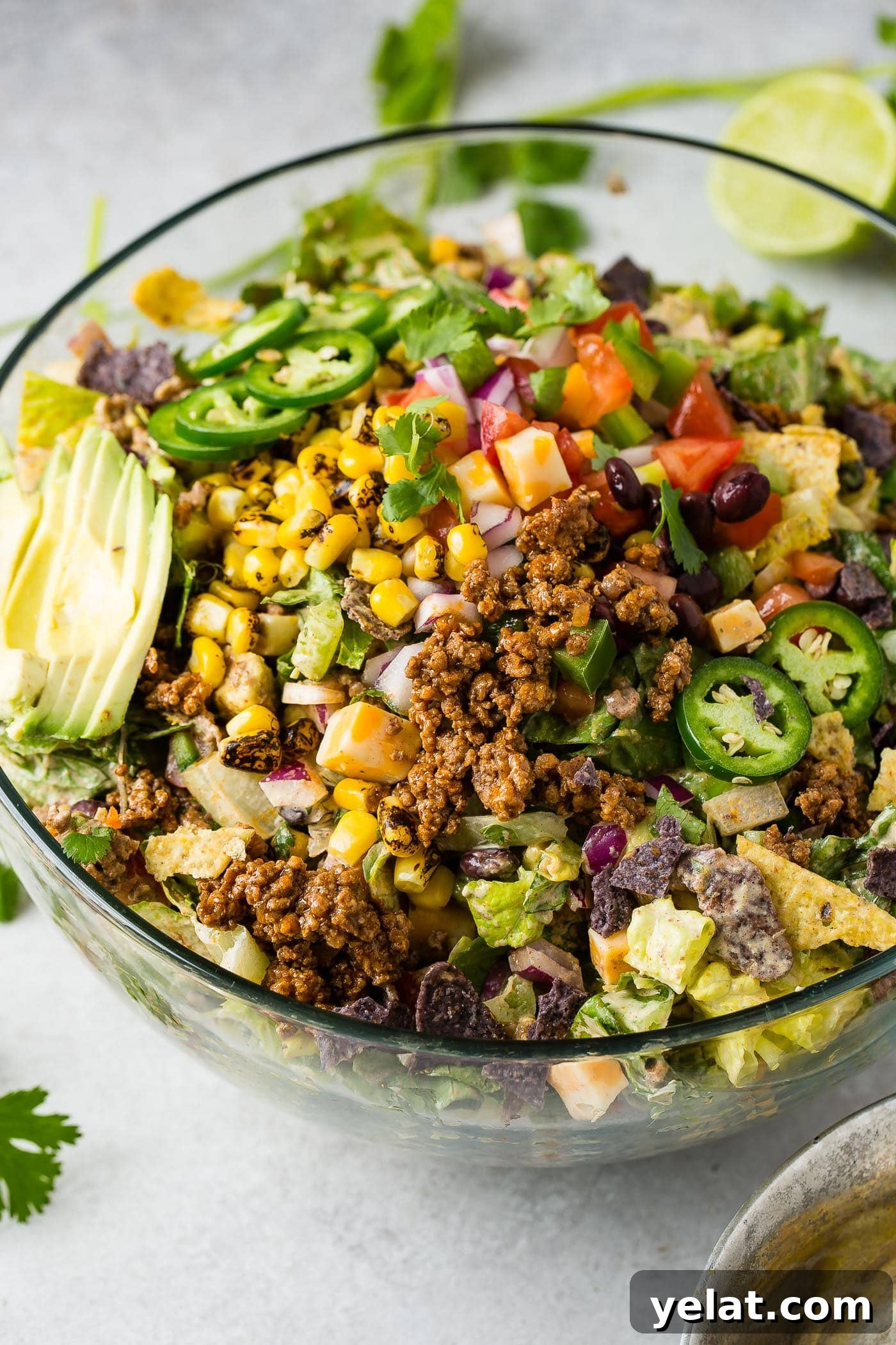 Tex-Mex Chopped Ground Beef Taco Salad Recipe 3 A glass bowl of tex‑mex taco salad. The salad is loaded with lettuce, taco meat, corn, tomatillas, tomatoes, taco meat, and has a sliced avocado on top.