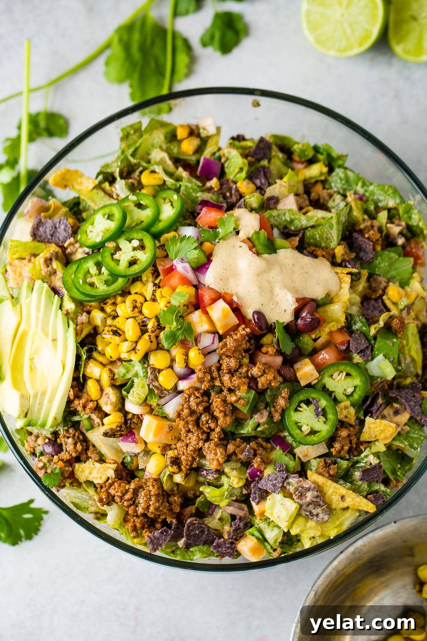 Tex-Mex Chopped Ground Beef Taco Salad Recipe 4 A top view of a large glass bowl of tex‑mex taco salad. It is loaded with lettuce, corn, avocado, tomatillos and taco meat. There is a little dressing poured in the top part of the salad.
