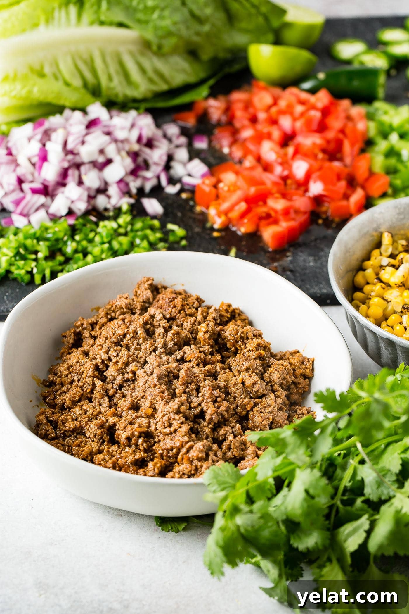 Tex-Mex Chopped Ground Beef Taco Salad Recipe 5 Ingredients for tex‑mex taco salad. There is a bowl of taco meat, a bowl of roasted corn, cilantro, chopped green bell peppers, chopped tomatoes, and chopped red onion.