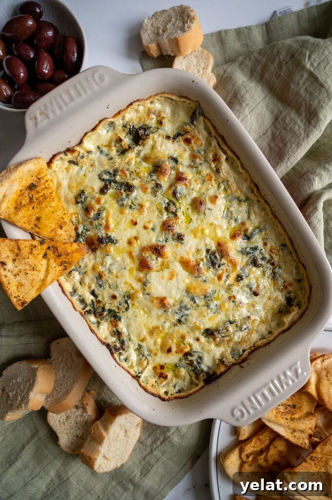 Baked spanakopita dip in a white casserole dish, with 2 baked pita chips on it.