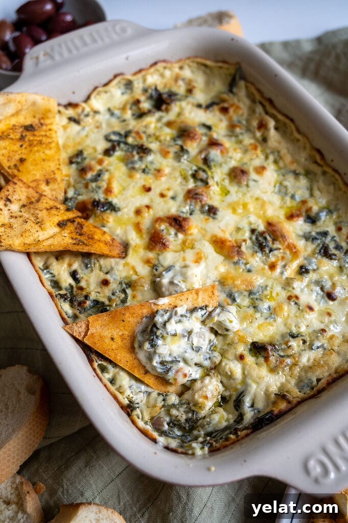 Baked spanakopita dip in a white casserole dish, with 3 baked pita chips on it.