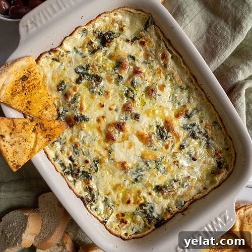 Baked spanakopita dip in a white casserole dish, with 2 baked pita chips on it.