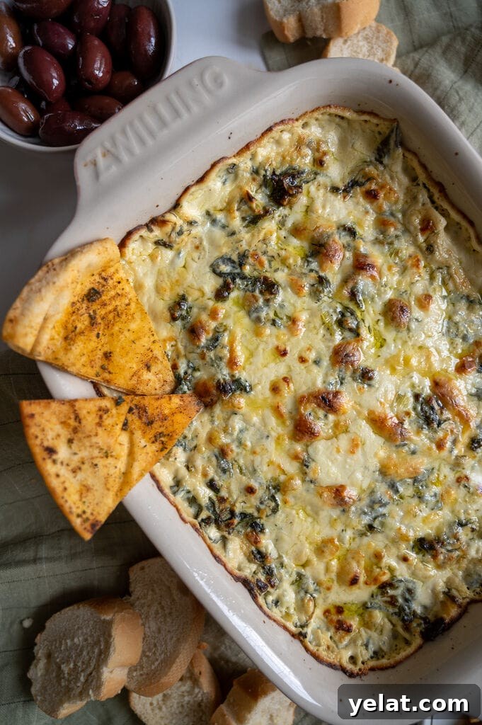 Baked spanakopita dip in a white casserole dish, with 2 baked pita chips on it.