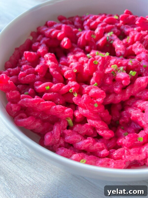 Polish Strawberry Pasta Recipe: Sweet Summer Noodles with Strawberries 5 A white bowl filled with vibrant Barbie Pasta, its bright pink hue garnished with chopped green herbs, sits on a light-colored surface.