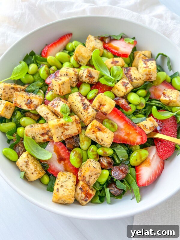Polish Strawberry Pasta Recipe: Sweet Summer Noodles with Strawberries 6 A bowl of The Kourtney Kardashian Salad with cubed tofu, sliced strawberries, edamame, greens, dates, and fresh basil leaves, artfully arranged on a white surface.