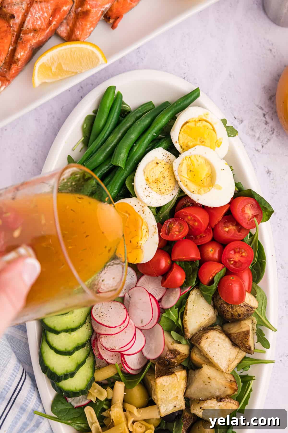 Dressing being poured over salmon Nicoise salad on a white platter.