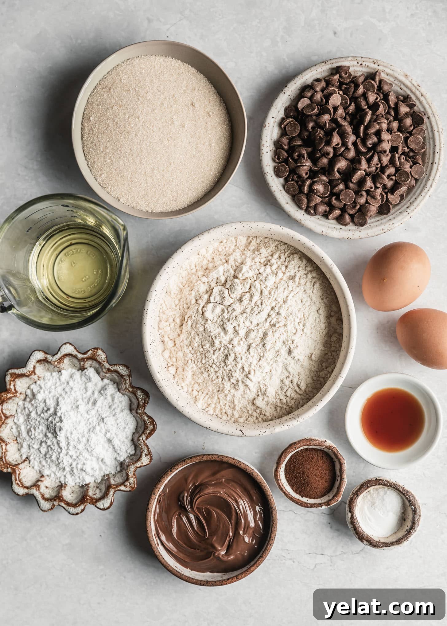 Fudgy Mocha Crinkle Cookies Recipe for Rich Chocolate Coffee Cookies 3 White and brown bowls of flour, powdered sugar, sugar, oil, vanilla, espresso powder, chocolate chips, and Nutella on a white counter next to eggs.